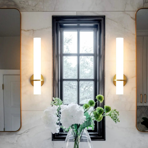 Two Pack Gold Bathroom Wall Sconces 18 Inch Modern LED Dimmable Wall Lights With Acrylic Lampshades Brushed Gold Finish For Bedroom Living Room Hallway Hardwired installed beside a window in a modern bathroom.