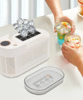Quick Chill Portable Ice Cube Maker For Home Or Car with ice cubes, compact white design, and two colorful drinks on table.