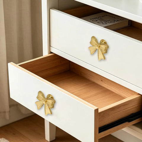 Six Piece Zinc Alloy Bow Drawer Knobs With Vintage Plating And Smooth Curved Handles For Dressers And Vanity Furniture Upgrades That Bring Main Character Energy To Your Space, gold pulls on white drawer.