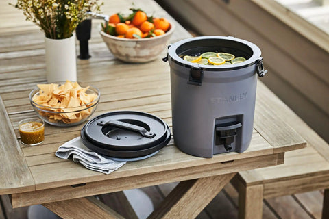 Adventure Fast Flow 2 Gallon Water Jug With Leakproof Ice Dispenser on outdoor table with snacks and fruits