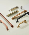 Assorted styles of handle pulls and knobs in various finishes, including matte black, bronze, and nickel, displayed on a light surface.