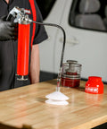 Side view of ARES bearing packer kit: red grease gun, hose, and two white cone-shaped packing cones on a wood table.