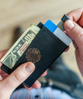 Person holding a slim black wallet with cash, cards, and a flower embellishment, emphasizing style and compactness.