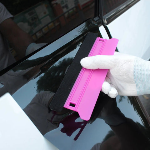 Vinyl Wrap Heat Gun Kit For Car Wrap And Window Tint Includes 110V 1800W Heat Gun Plastic Squeegees Magnetic Holder Gloves And Smoothing Tools For Quick Film Stretching And Perfect Finish displaying pink plastic squeegee used on car window.