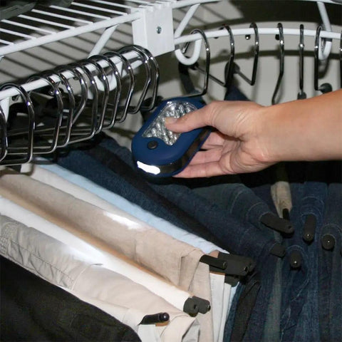 Hand holding Magnetic LED Work Light Six Pack With 27 LED Lights And Swivel Hook, illuminating clothes in closet.