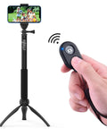 Hand holding Two Pack Wireless Phone Camera Remote Shutter For iPhone And Android With Wrist Strap, tripod and smartphone in background.