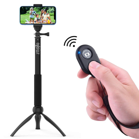 Hand holding Two Pack Wireless Phone Camera Remote Shutter For iPhone And Android With Wrist Strap, tripod and smartphone in background.