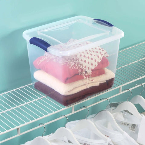 Twenty Seven Quart Clear Plastic Storage Container With Durable Blue Latches And Secure Recessed Lid Stackable Tote Bin For Hassle Free Home Organization Real Deal on a closet shelf with folded clothes.