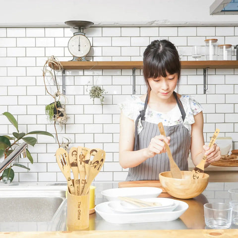 Woman cooking with TV Show Themed Wooden Spoons Set With Holder, 6 Piece Kitchen Utensils For Cooking And Serving, Nonstick Safe.
