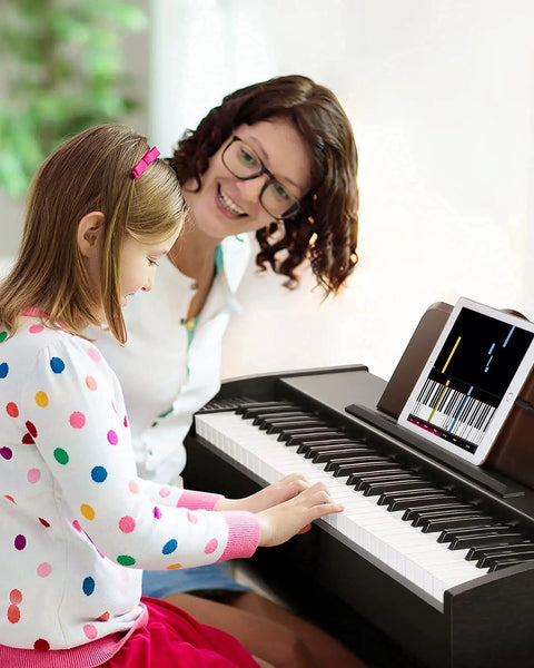 Child playing 61 Key Starter Keyboard Piano With Classic Wooden Frame Electric Digital Piano Sustain Pedal Music Stand USB MP3 Audio Mic and Headphone Support Kid Friendly Gift For Girls Daughter Birthday while adult watches.