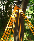 Close-up of vibrant orange outdoor nylon rope hammock swing attached to tree, mesh seat visible.