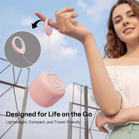 Ultra Portable Bluetooth Speaker With Strap For On The Go IPX5 Waterproof Mini Speaker That Bangs With Loud Stereo Sound 20 Hours Of Playtime Rechargeable Battery Built In Microphone Pink being held outdoors.