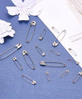 450 Pack Real Deal Iron Safety Clasp Pins For Crafting And Tailoring displayed on blue background with paper flowers.