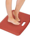 Feet standing on a red 18x22 inch Anti Fatigue Standing Desk Floor Mat For Home Office Kitchen Garage, cushioned and non-slip surface.