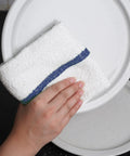 Hand using 16x19 inch terry cloth rag to clean plate; part of Value Pack Of 36 Absorbent 16x19 Inch Terry Cloth Cleaning Rags For Home And Business.