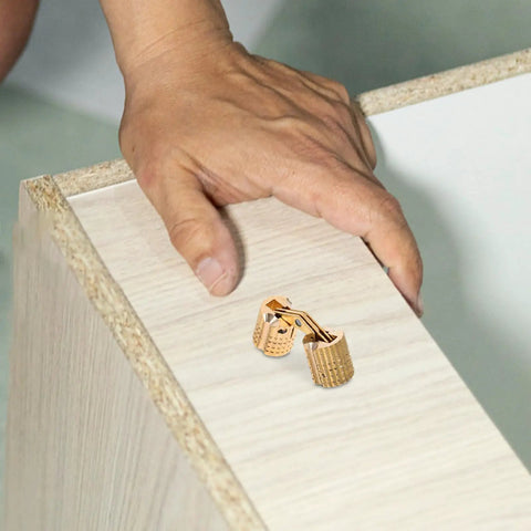 Smooth Operator Brass Concealed Barrel Hinges Six Piece Kit on a wooden cabinet with a hand, showcasing 180 degree folding design.