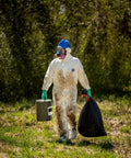 Person wearing a Disposable Protective Coverall With Respirator-Fit Hood And Elastic Cuffs, White, Medium, carrying waste outdoors