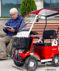 No Sweat Electric Mobility Scooter For Adults And Seniors With 28 Mile Range And 12 Mph Top Speed Hella Tough Frame parked beside a man reading.