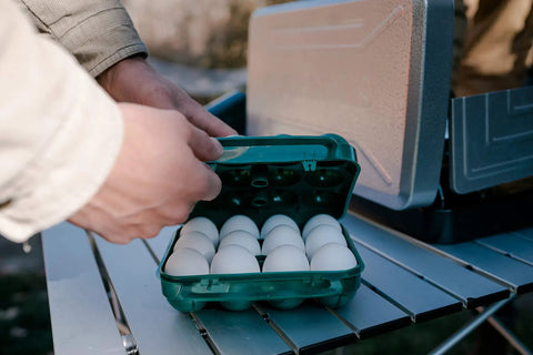 Hands securing Tough 12-Egg Plastic Carrier With Locking Lid, Molded Handle, And Secure Fit For Camping, Road Trips, And Meal Prep on table.