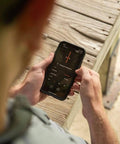 Person holding smartphone with app controlling settings of Behind The Neck Bluetooth Hearing Enhancer For Hunters With Retractable Earbuds