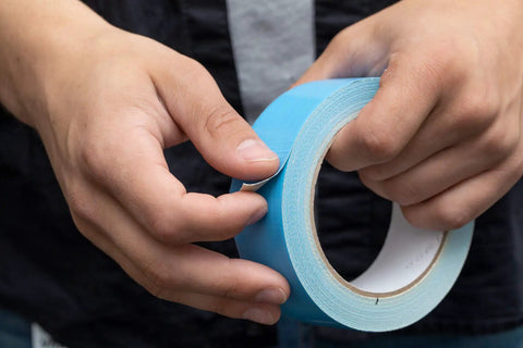 Hands holding a Blue Double Sided Duct Tape Roll 1.4 Inch By 12 Yards With Aggressive Natural Rubber Adhesive On Durable Woven Cotton Cloth.