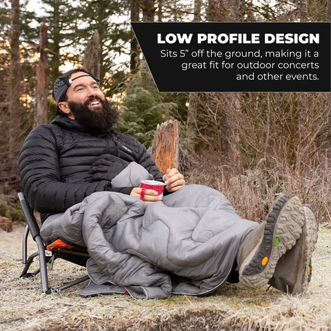 Man sitting outdoors on Low Profile Folding Camping Chair With Carry Bag Lightweight Breathable Mesh Seat For Camping Beach Picnic Barbecues And Sporting Events Easy Transport And Cushioned Armrests Black, wrapped in a blanket.