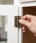 Hand installing 12 Pcs Small Antique Bronze Iron Cabinet Hinges 1.4 Inch with Rounded Corners on a white cabinet door.