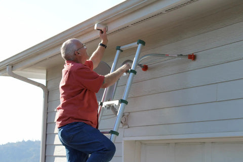 Man uses Heavy Duty Ladder Stabilizer for safer roof access and gutter protection. Fits most ladders, 19 inch safe work area.