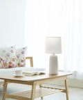 Textured Linear Ceramic Table Lamp In Off White With White Fabric Shade Pottery Style Cozy Vibe Uses 60W A19 Bulb on wooden table