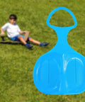 Blue Snow Sled For Kids And Adults against grass, downhill toboggan sledge for winter fun, flexible PP plastic, non slip seating