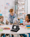 Children gathered around a table with a 58mm Button Maker Circle Cutter Punch For Badges And DIY Crafts, sturdy metal base visible.