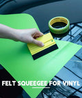Front view of neon green vinyl wrap sheet pressed with a yellow felt squeegee on a car hood; FOSHIC tape roll nearby.