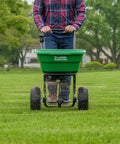 Person using Walk-Behind Broadcast Spreader for Fertilizer, Grass Seed and Salt, 80 Lb Hopper with 12-Inch Knobby Pneumatic Tires