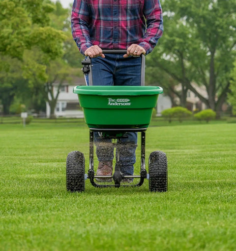 Person using Walk-Behind Broadcast Spreader for Fertilizer, Grass Seed and Salt, 80 Lb Hopper with 12-Inch Knobby Pneumatic Tires