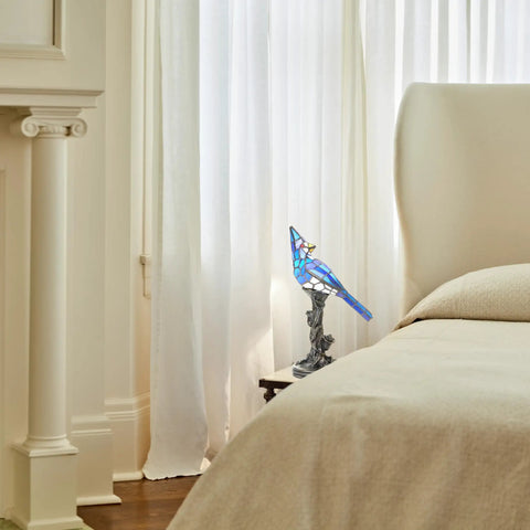 Stained Glass Bird Accent Lamp With Blue Jay Design Tiffany Style Table Lamp 8 W X 13.5 H Inches Bronze Tree Trunk Base Blooming Flowers Vintage Look Cozy Living Room Nightstand Decor by a bedside in warmly lit room