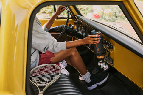 Person holding a Rock Solid Leakproof Shaker Bottle With Connected Hinge Cap And Fast Flow Spout in a vintage car interior.