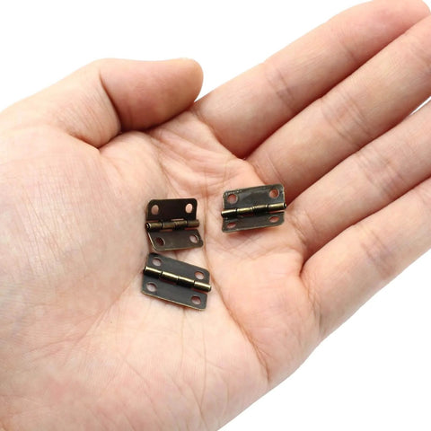Hand holding three Bronze Mini Jewelry Box Hinges Set Of 60 With Screws For Diy Projects And Crafts On Wooden Boxes And Cases Antique 