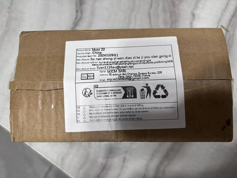 Cardboard package with shipping label placed on a marble surface, showing addresses and recycling symbols.