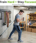 Man using gym gear next to 8 Hook Wall Mount Home Gym Organizer Rack for Barbells Resistance Bands Jump Ropes Foam Rollers Belts