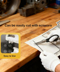 Gasket paper sheet being cut with scissors on a workbench; high-temp non-asbestos gasket material for small engines.