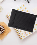 Black padded bubble mailer next to polka dot notebooks and a donut, part of 100 pack, 12x18 padded bubble mailers self seal envelopes.