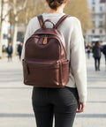 Person wearing a brown leather backpack with decorative zipper tabs visible, standing in an urban setting.