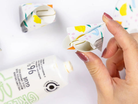 Hand holding a paper craft with floral patterns, using glue from tube labeled 96% natural ingredients.