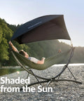 Set Up In 3 Seconds Adjustable Portable Aluminum Hammock Stand For Outdoors with canopy on rocky beach, man relaxing.