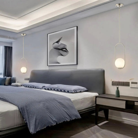 Modern bedroom with pendant ceiling lights, featuring sleek bed and decor under soft illumination.