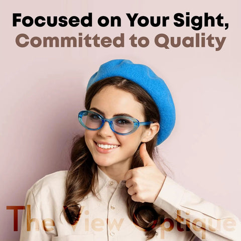 Blue-framed eyeglasses on smiling woman wearing a blue beret; pink backdrop with The View Optique watermark.