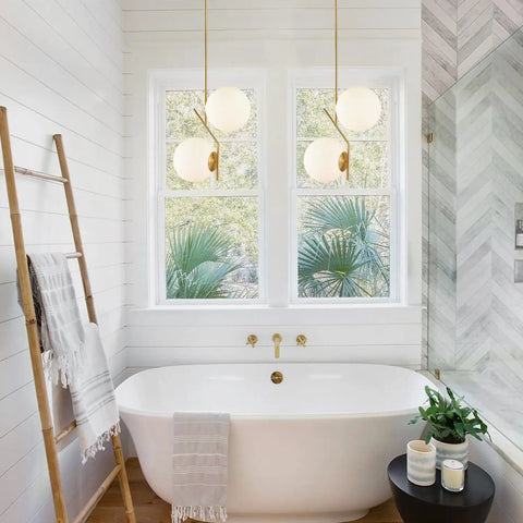 Two Light Glass Globe Pendant Light In Brushed Brass Gold Finish Modern Mid Century Style over a white bathtub