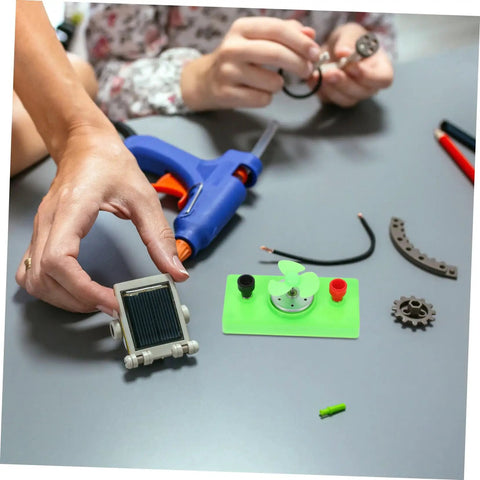 Hands assembling Mini Solar Powered DC Motor For Science Experiments And Hands On DIY Projects with tools and parts on table.