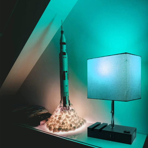 RGB Smart Table Lamp With Remote Control Alexa Voice And App Control Music Sync Dimmable Nightstand Lamp With Charging Station next to a rocket model on a shelf.