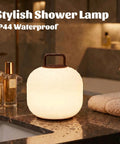 Cordless RGBW LED Table Lamp With Remote Control on a bathroom counter, IP44 waterproof for shower use, glowing softly.